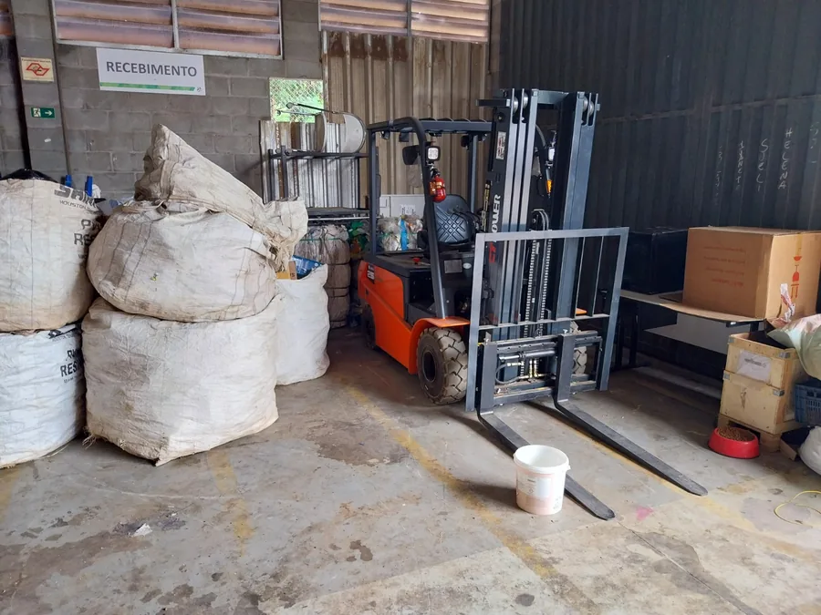 Área de recebimento da cooperativa, com bags de material e empilhadeira elétrica