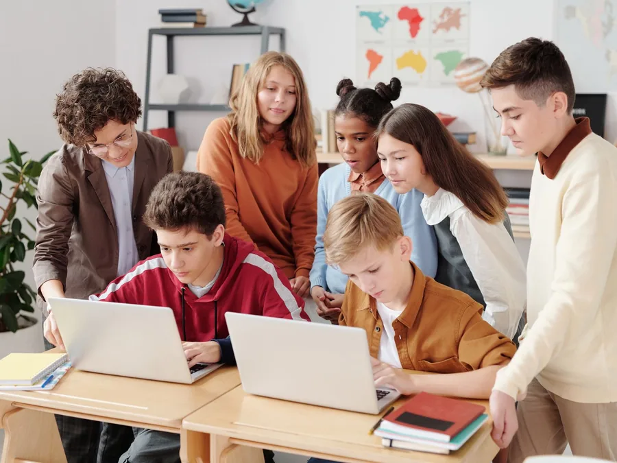 Jovens em volta dos computadores durante uma aula, com o professor acompanhando